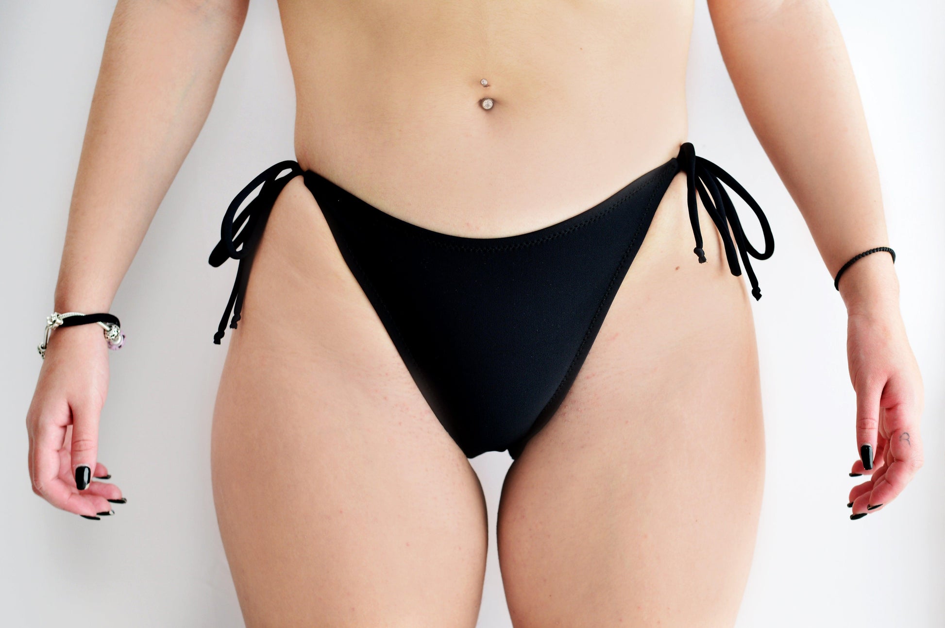 Sunlover Swimwear model wearing a classic black bikini bottom with ties on a plain background (Colour: BLK)