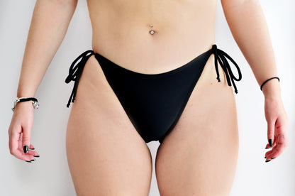 Sunlover Swimwear model wearing a classic black bikini bottom with ties on a plain background (Colour: BLK)